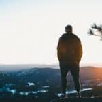 man standing on cliff mountains overview